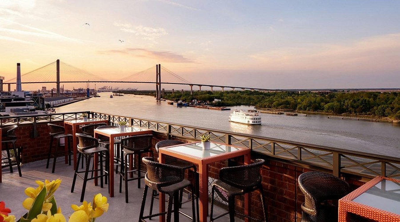 Empty waterfront dining tables at dusk overlooking a river and bridge